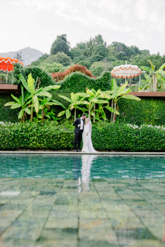 Hochzeitslocations am Comer See: 10 Luxus-Villen & Luxushotels mit direktem Seeblick am Comer See 14 Eine Braut und ein Bräutigam stehen bei ihrer verträumten Hochzeit am Pool, umgeben von üppigem Grün und bunten Sonnenschirmen, und fangen die Romantik Apuliens ein.