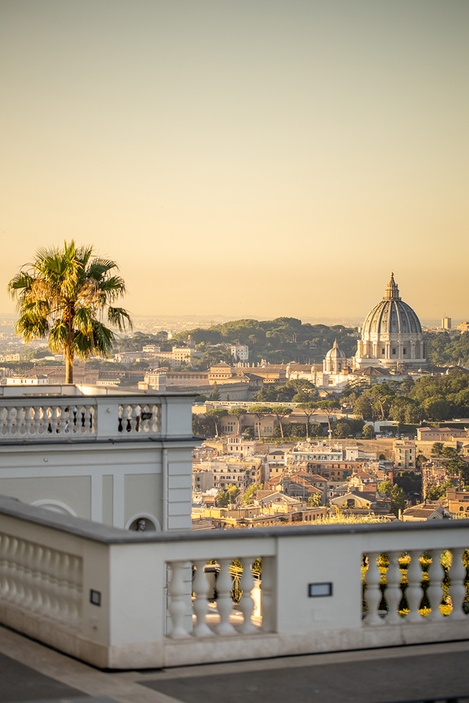 Villa Miani Rom: Heiraten in der Hochzeitslocation mit Blick über Rom 3 Panoramablick auf Rom mit einer Palme und der Kuppel des Petersdoms in der Ferne bei Sonnenuntergang.
