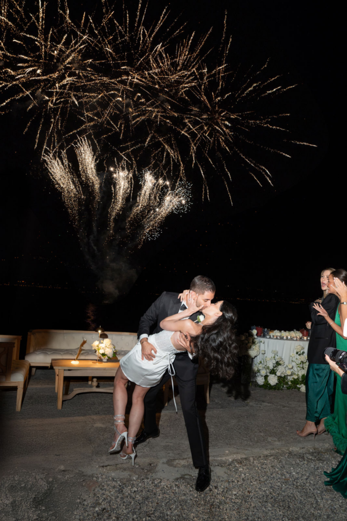 Heiraten am Gardasee, Italien - Alle Infos, Kosten & Hochzeitslocations 27 Ein Paar küsst und tanzt unter einem nächtlichen Feuerwerk am Comer See, umgeben von formell gekleideten Gästen - ein unvergesslicher Moment, der von einem erfahrenen Hochzeitsplaner geschaffen wurde.
